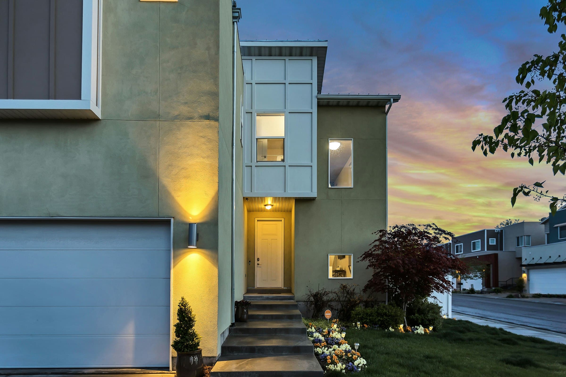 A two-story house at twilight, porch lights on beneath a violet sky